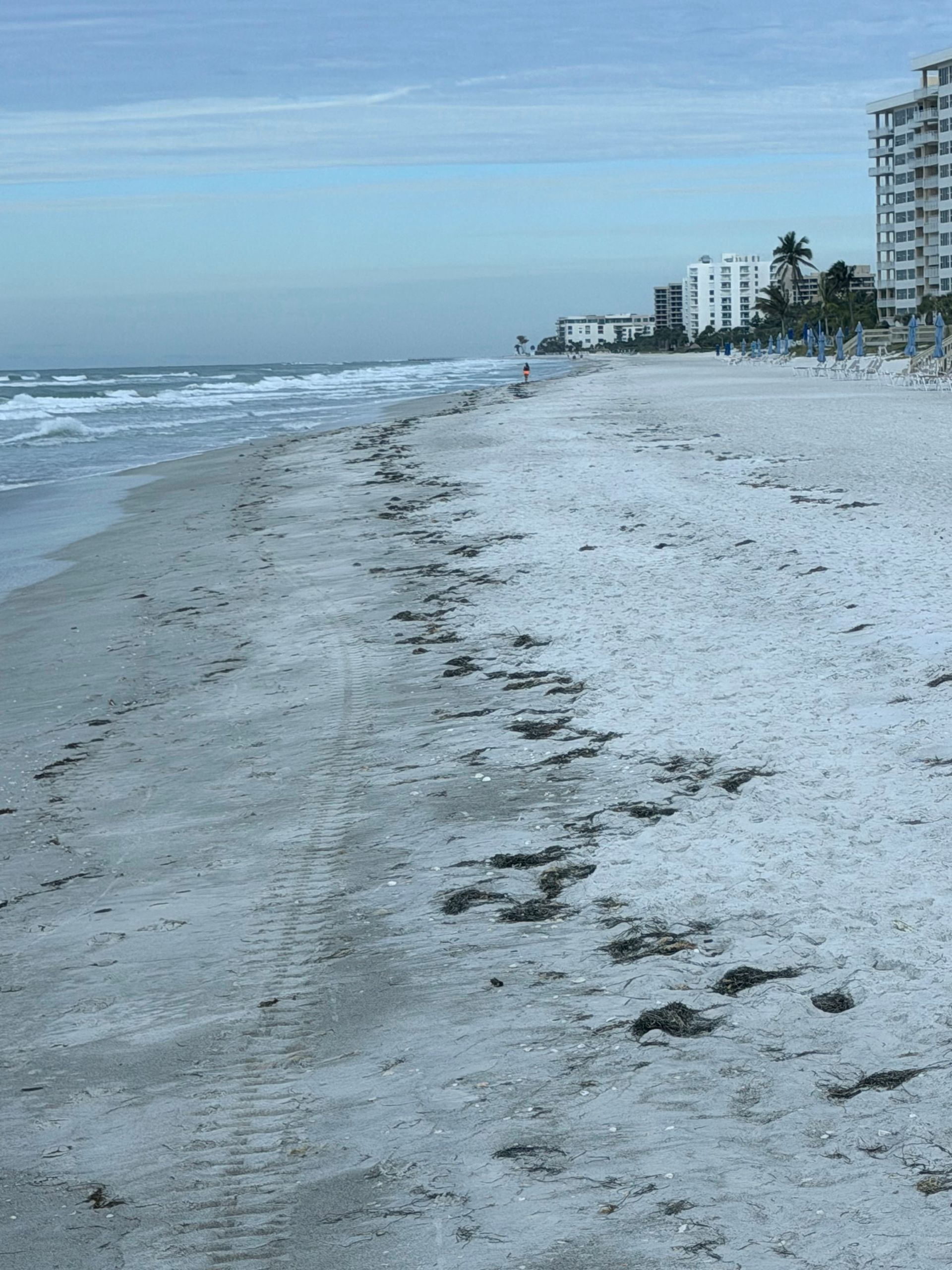 Beach with footprints leading to buildings on a cloudy day.