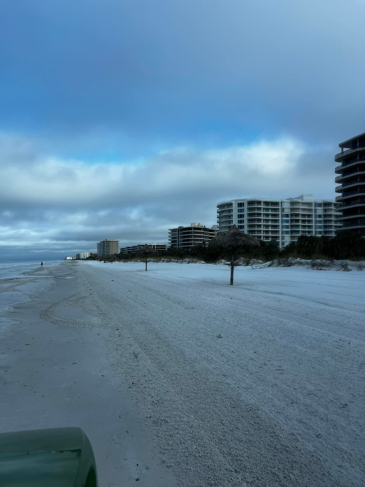 Beach scene with white sand, ocean, buildings, and a cloudy sky.