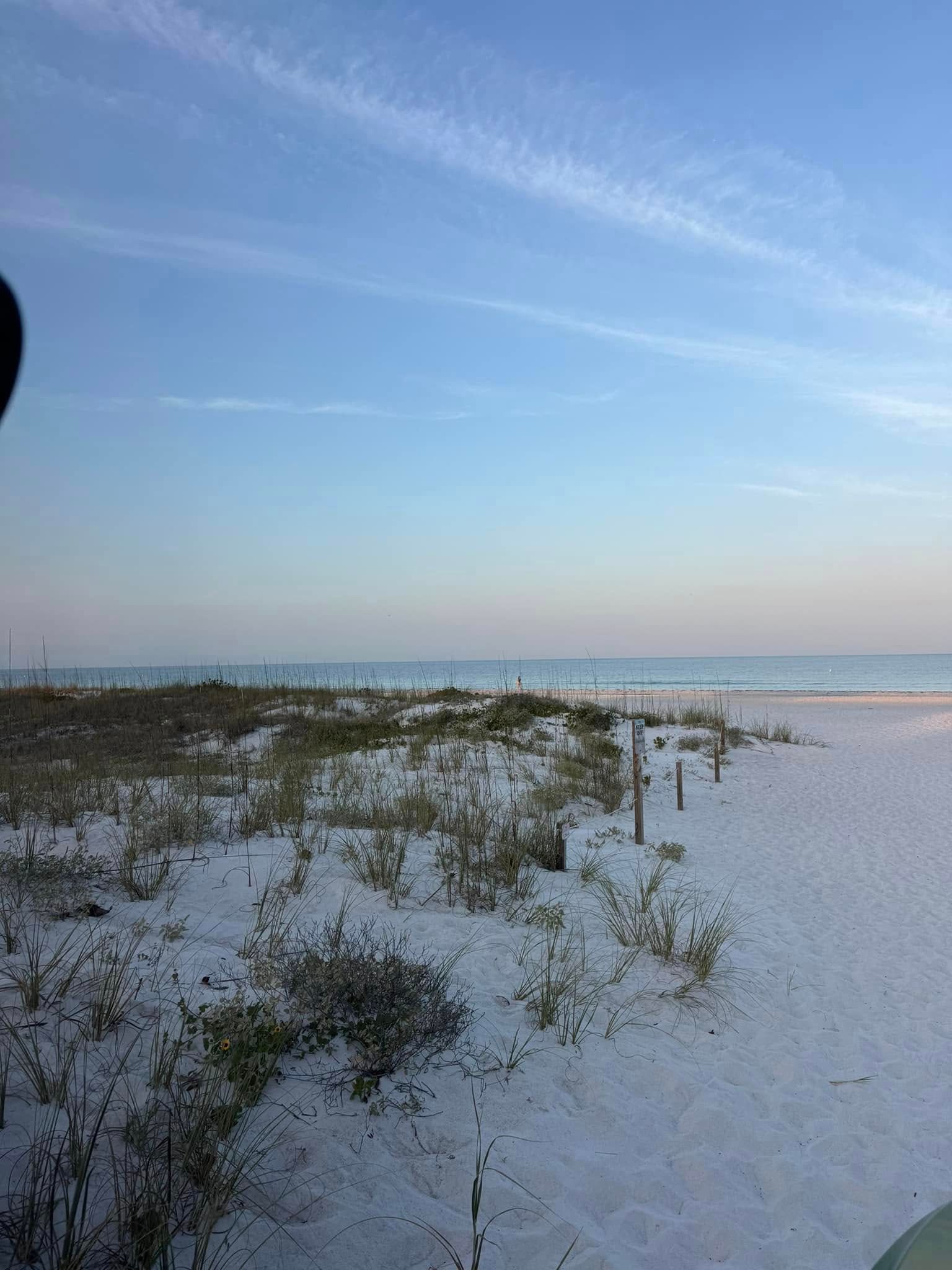 Beach scene with white sand, dune grass, blue sky and ocean.