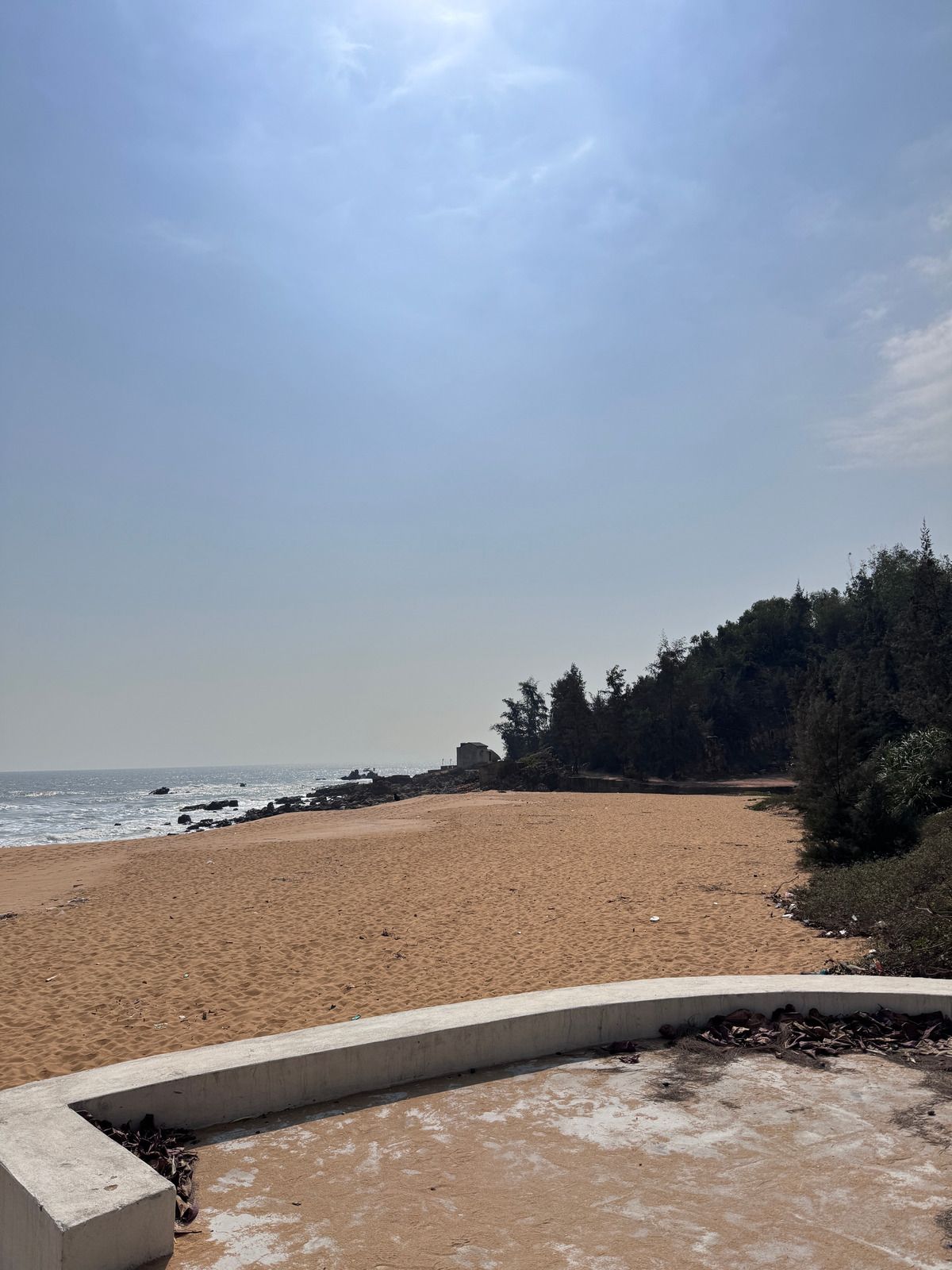 Green John Deere tractor pulling a hay rake on a dirt field with trees in the background under a blue sky.