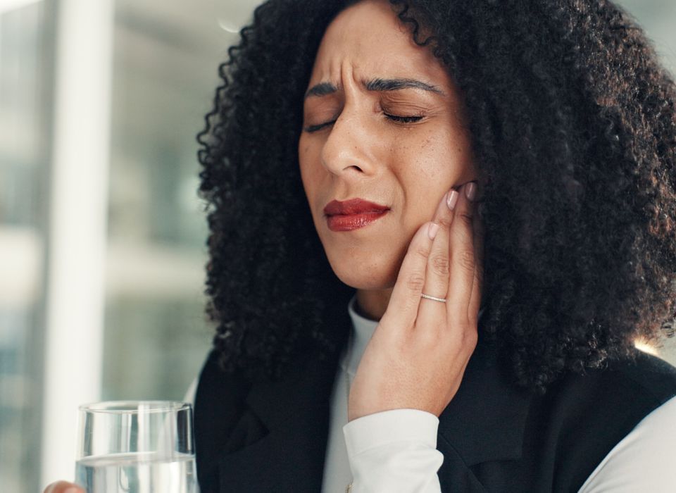 Woman holding cheek, eyes closed, appearing to be in pain, with a glass of water.