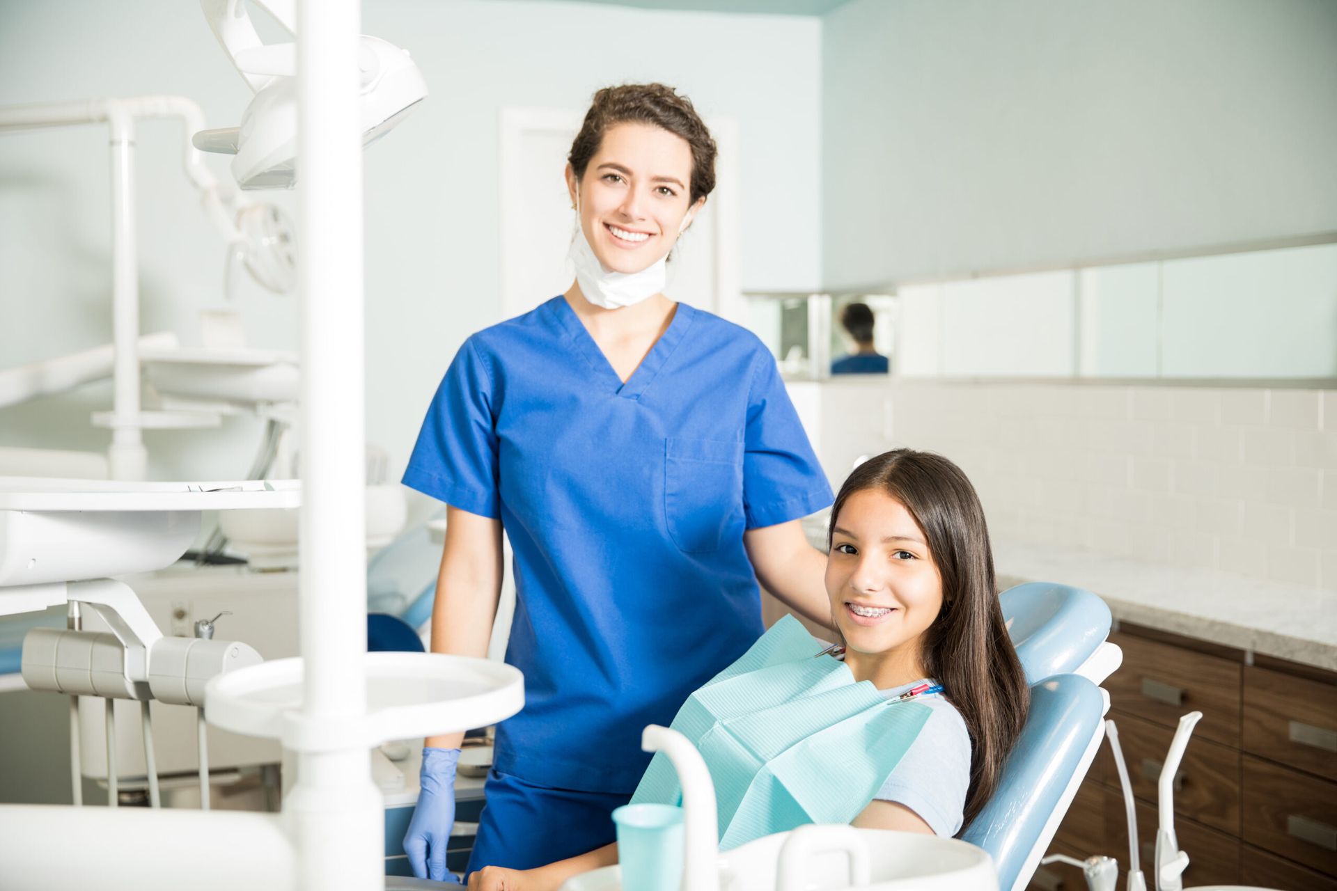 Dentist in blue scrubs with a patient in a dental chair, both smiling in a dental office.