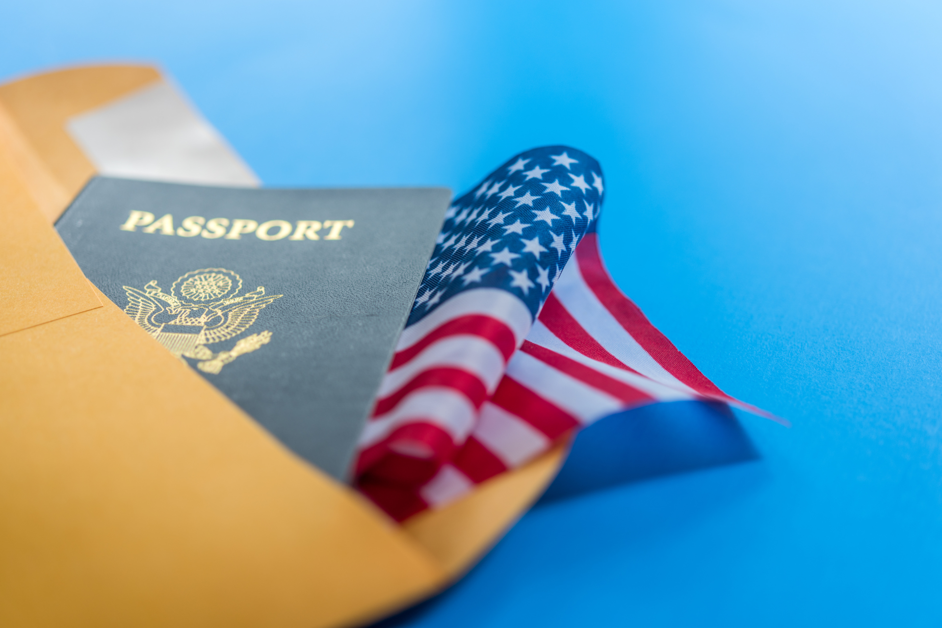 An american flag is sticking out of an envelope next to a passport.