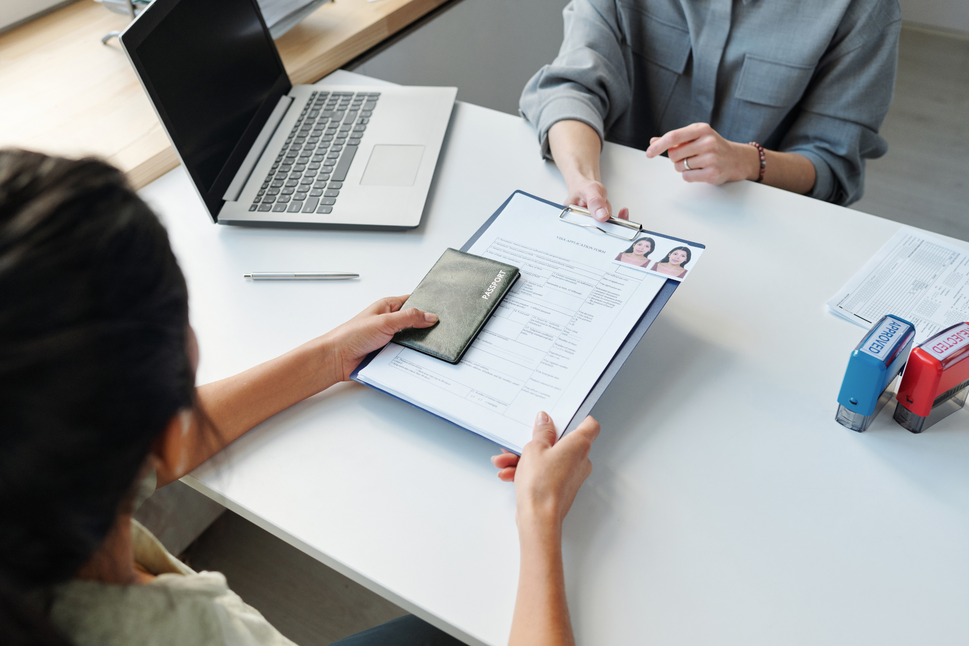 Two women are sitting at a table with a laptop and a clipboard.