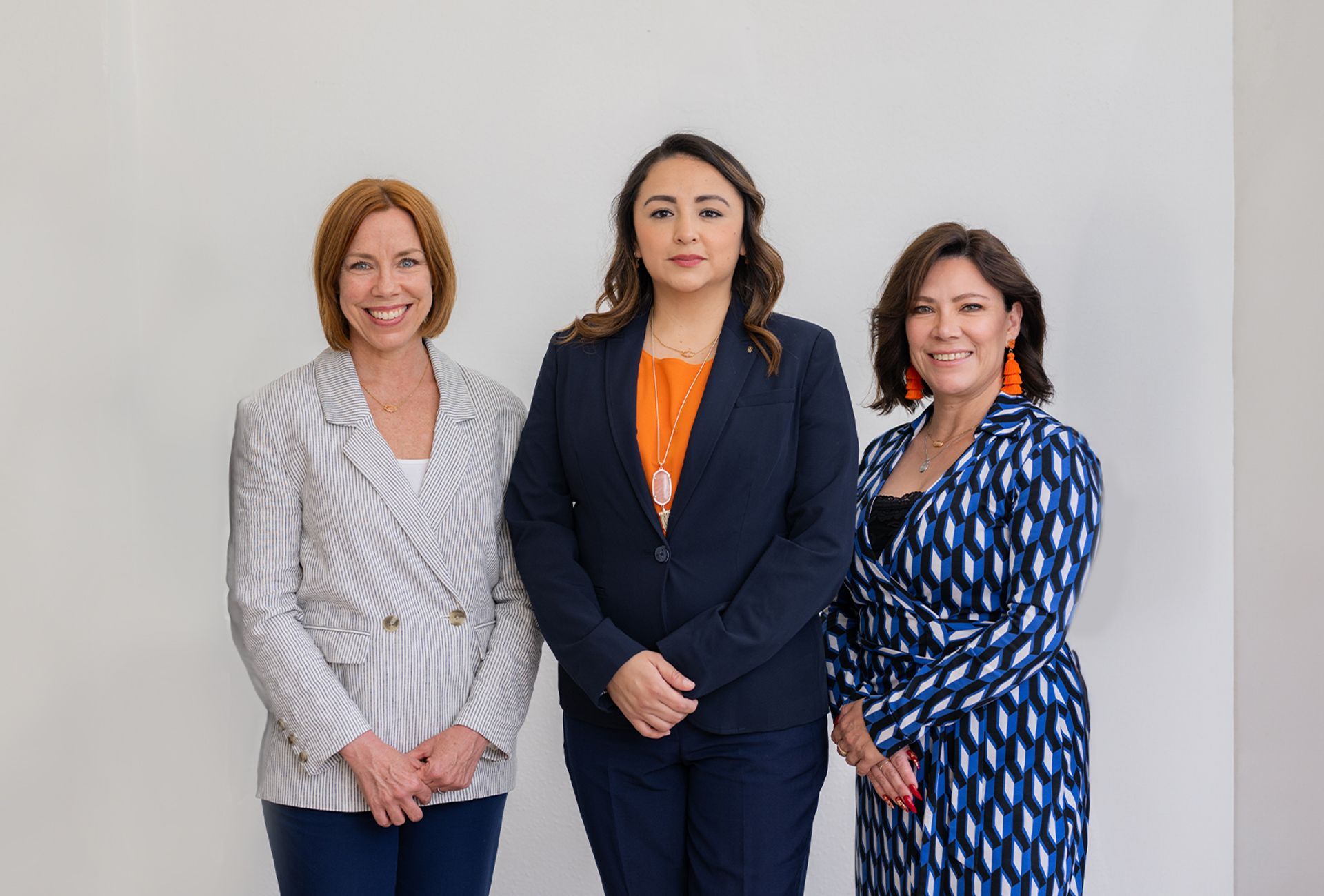 Three women are standing next to each other in front of a white wall.