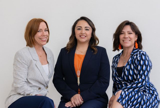 Three women are sitting next to each other and smiling for a picture.