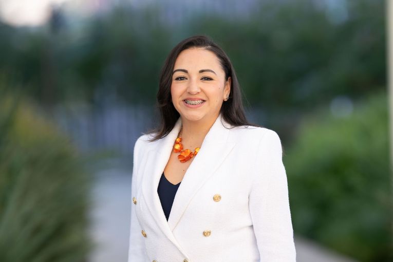 A woman in a blue jacket and orange shirt is smiling for the camera.