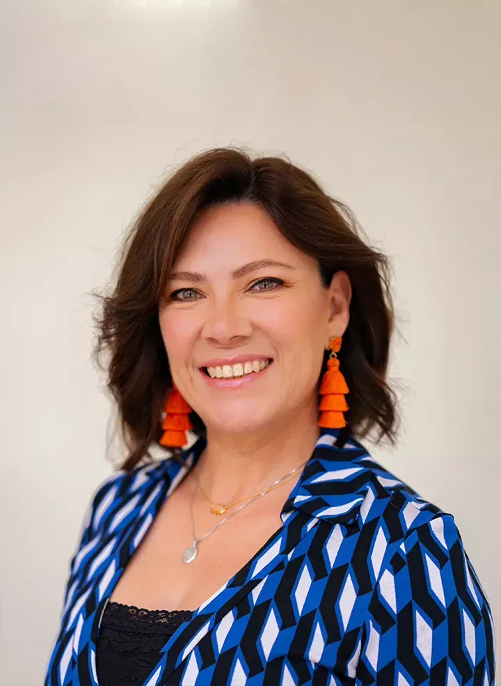 A woman wearing a striped jacket and a necklace is smiling for the camera.