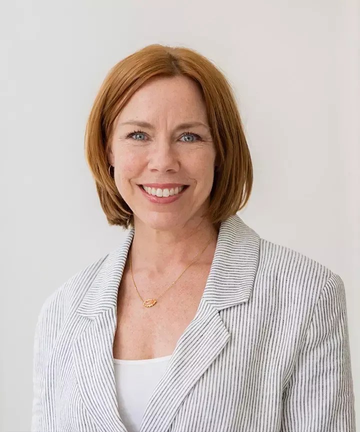 A woman wearing a striped jacket and a necklace is smiling for the camera.