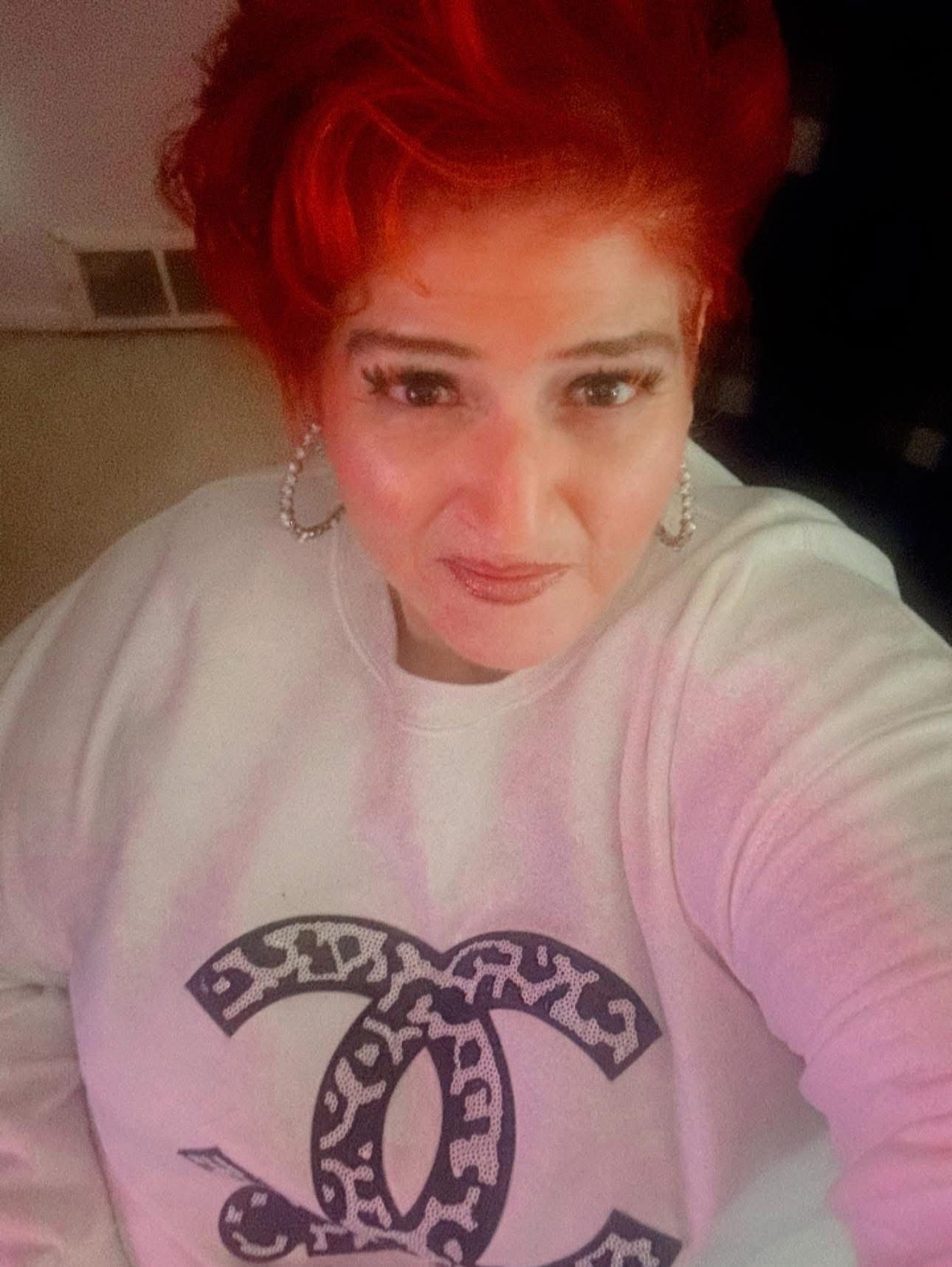 A woman with red hair is wearing a hat and earrings.