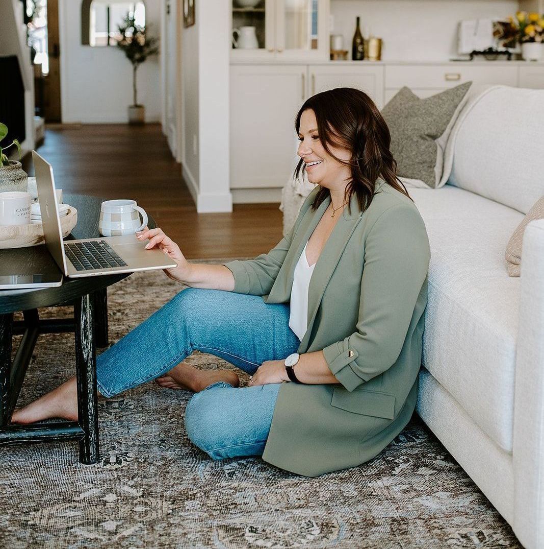 Megan Atamanik is sitting on the floor using a laptop computer.