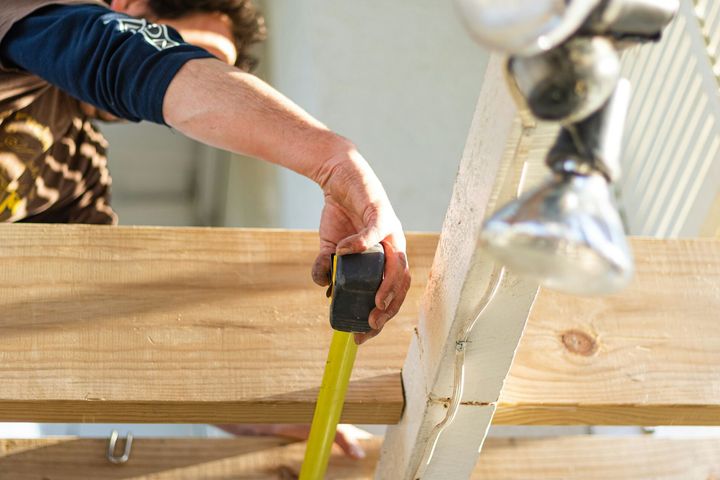 Person measuring a wooden board with a tape measure on a workbench