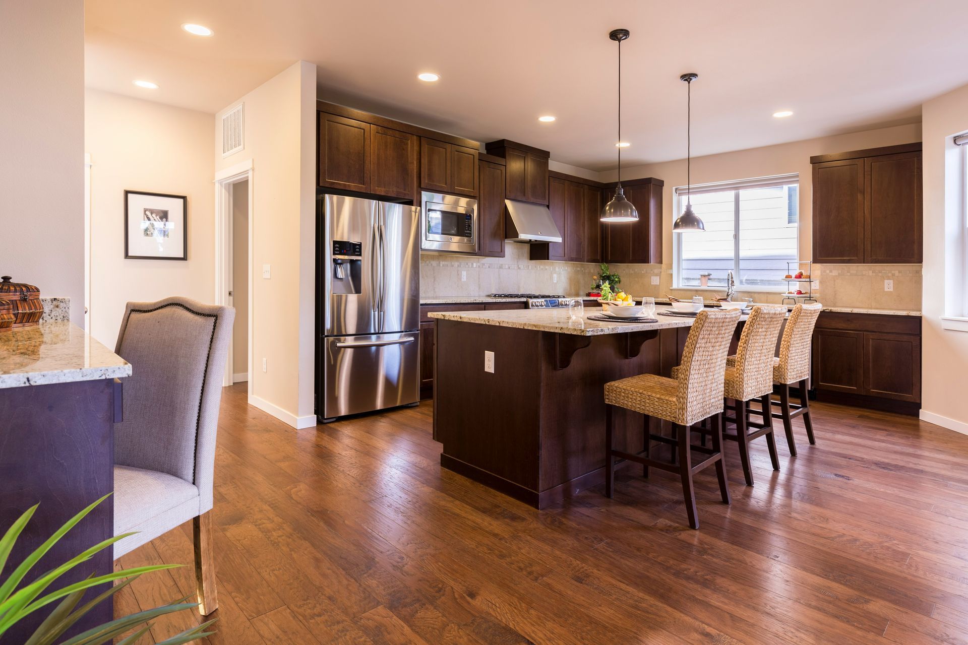 Modern kitchen with stainless steel appliances, dark wood cabinets, island, and bar stools in an open-concept home.