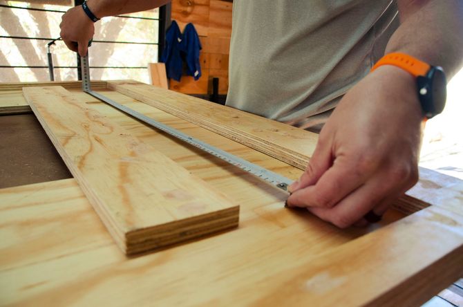 Person measuring a wooden board with a tape measure on a workbench