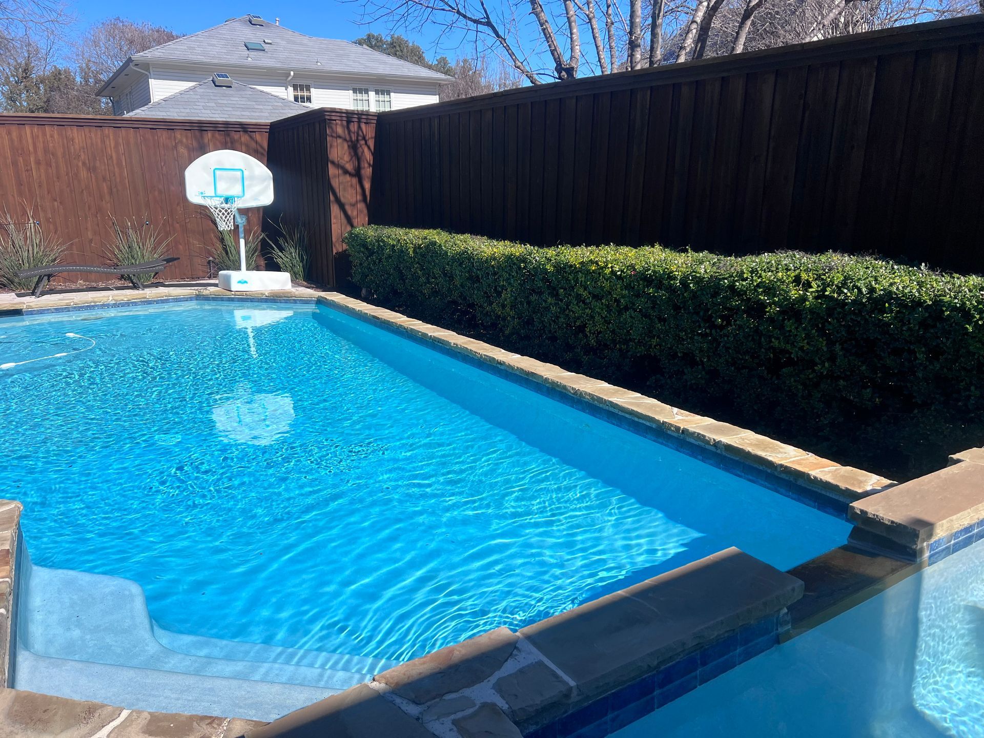 A large swimming pool with a basketball hoop in the backyard.