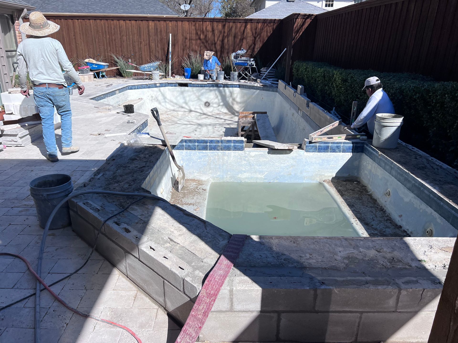 A man in a hat is standing next to a swimming pool under construction.