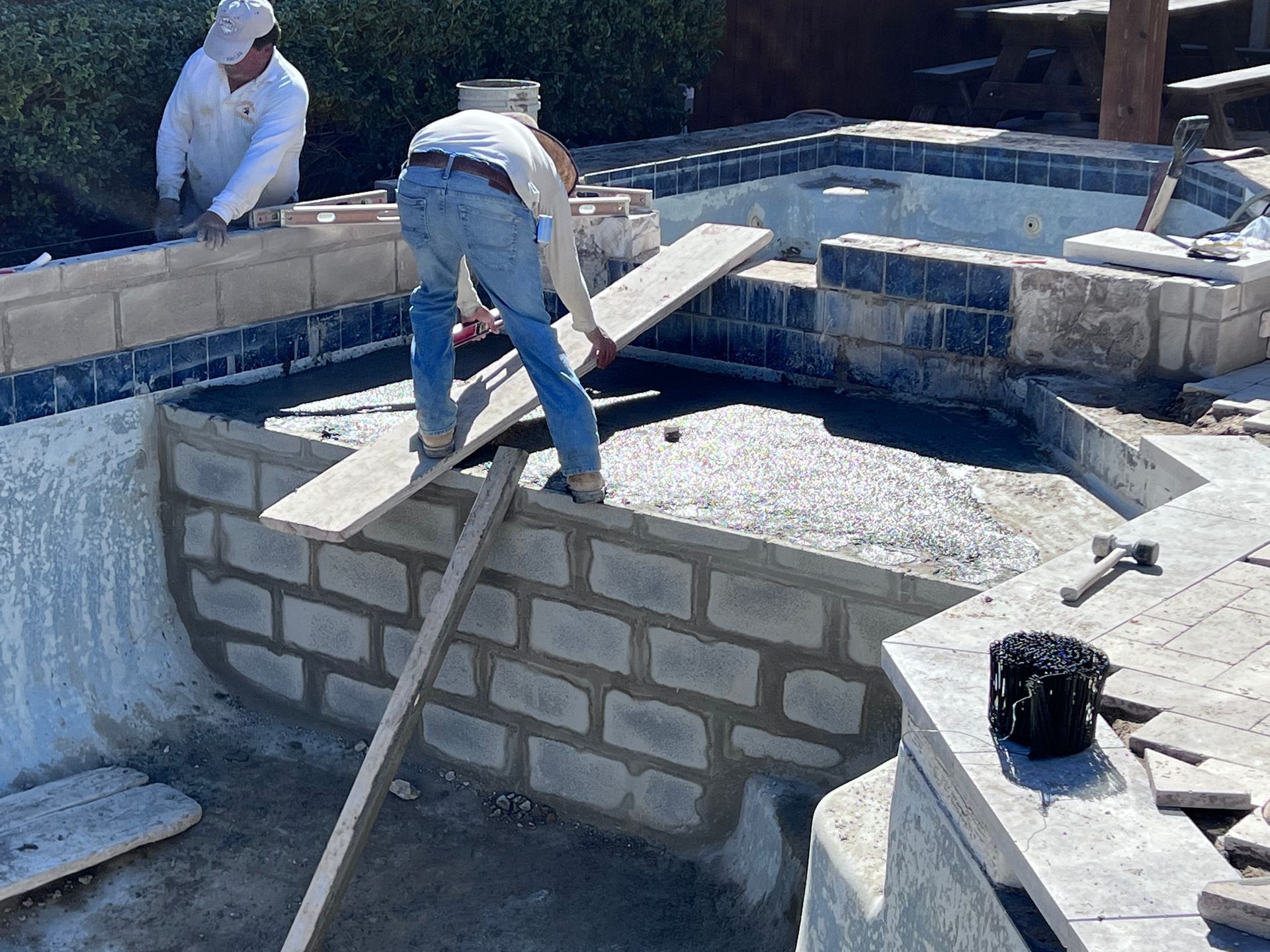 Two men are working on a brick wall around a pool.