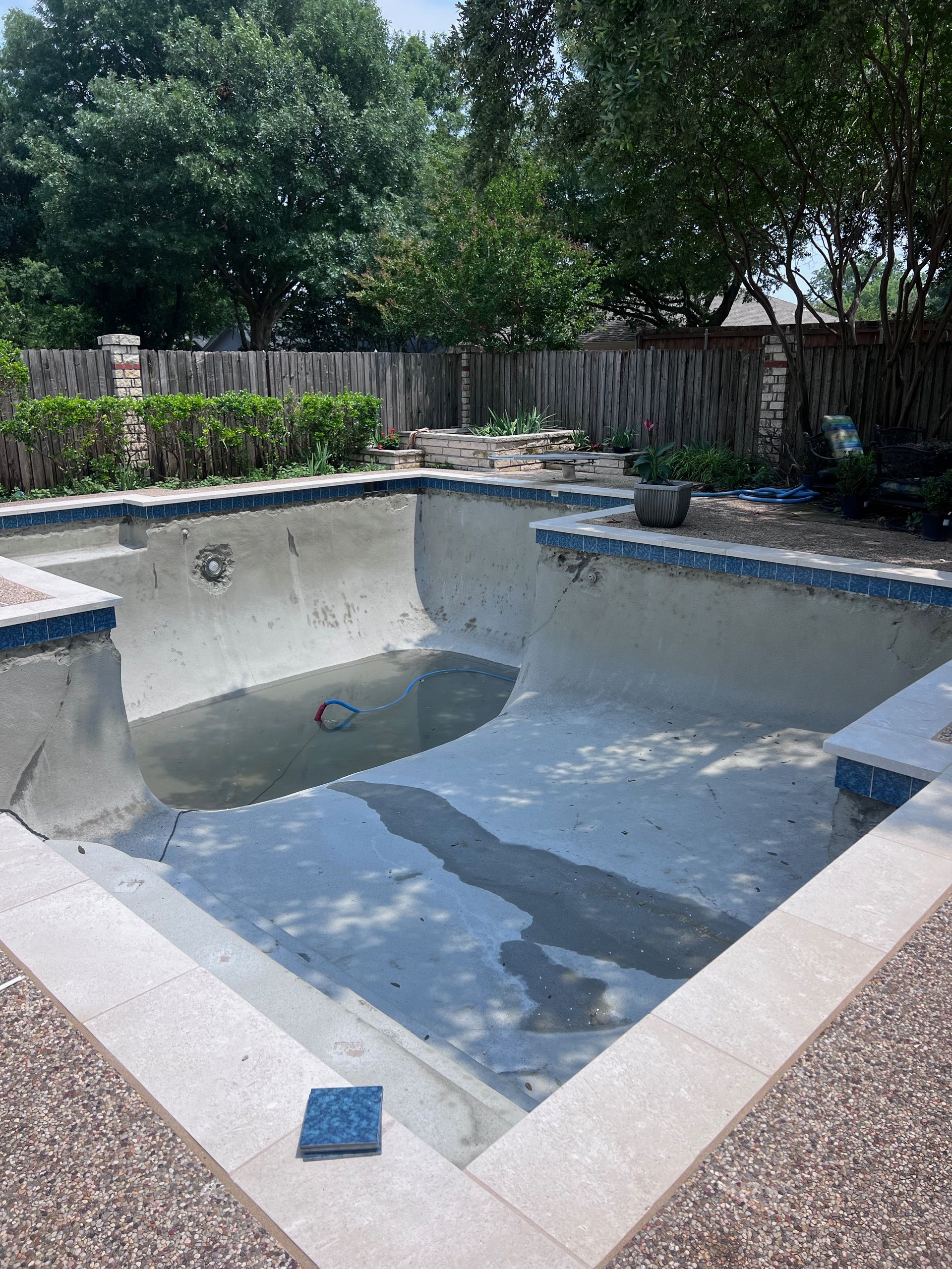 An empty swimming pool in a backyard with a fence in the background.