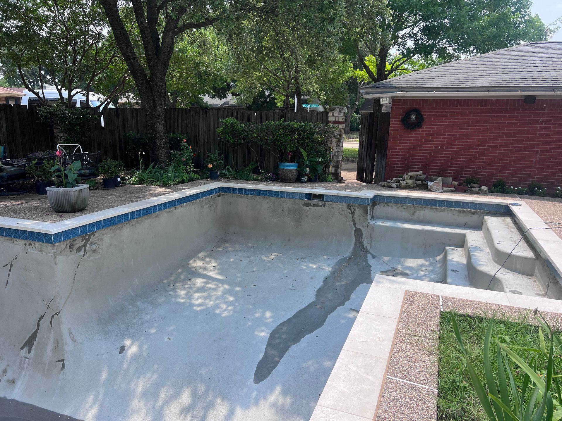 An empty swimming pool in a backyard with a brick building in the background.