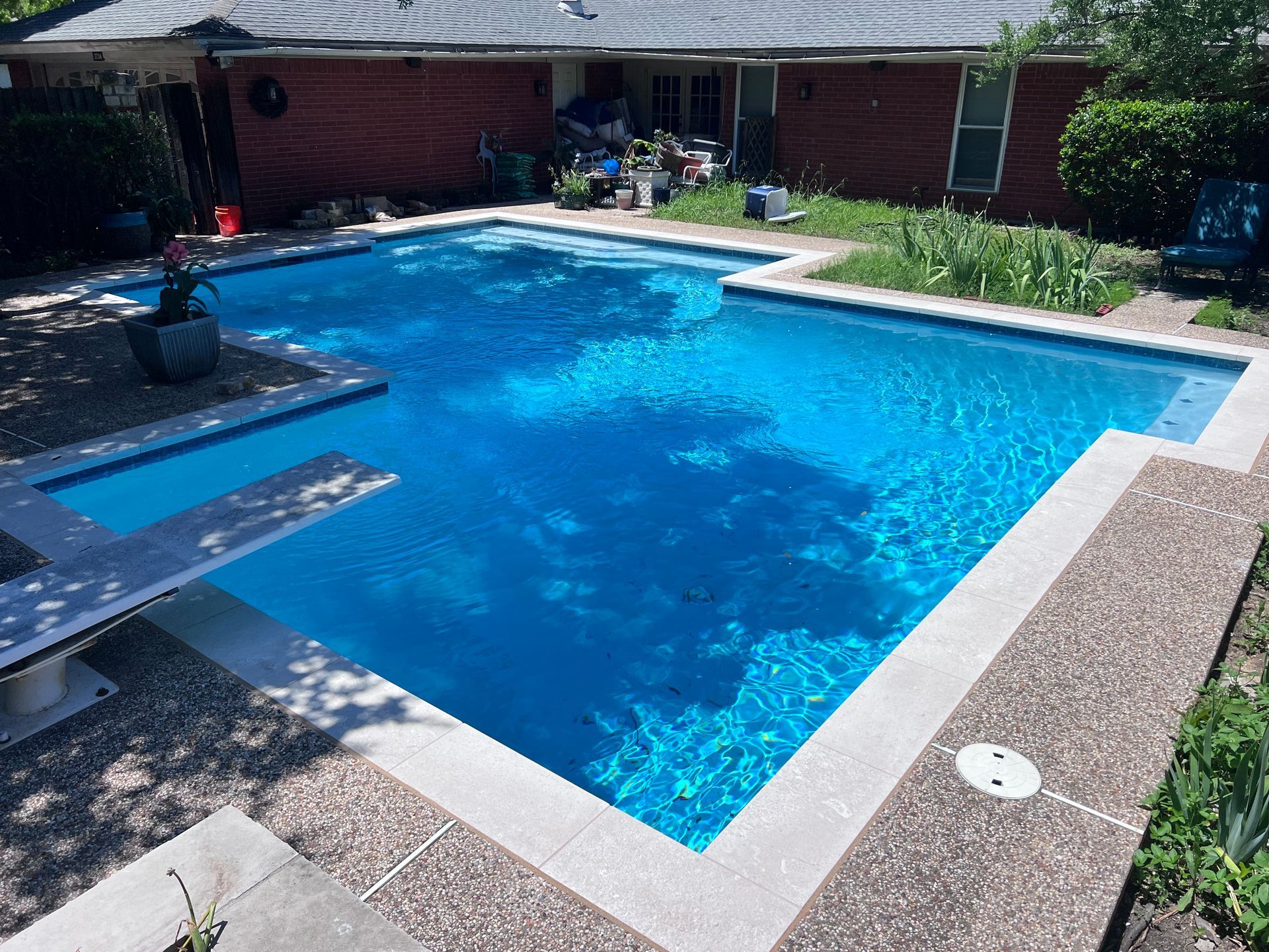 A large swimming pool with a diving board in front of a brick house.
