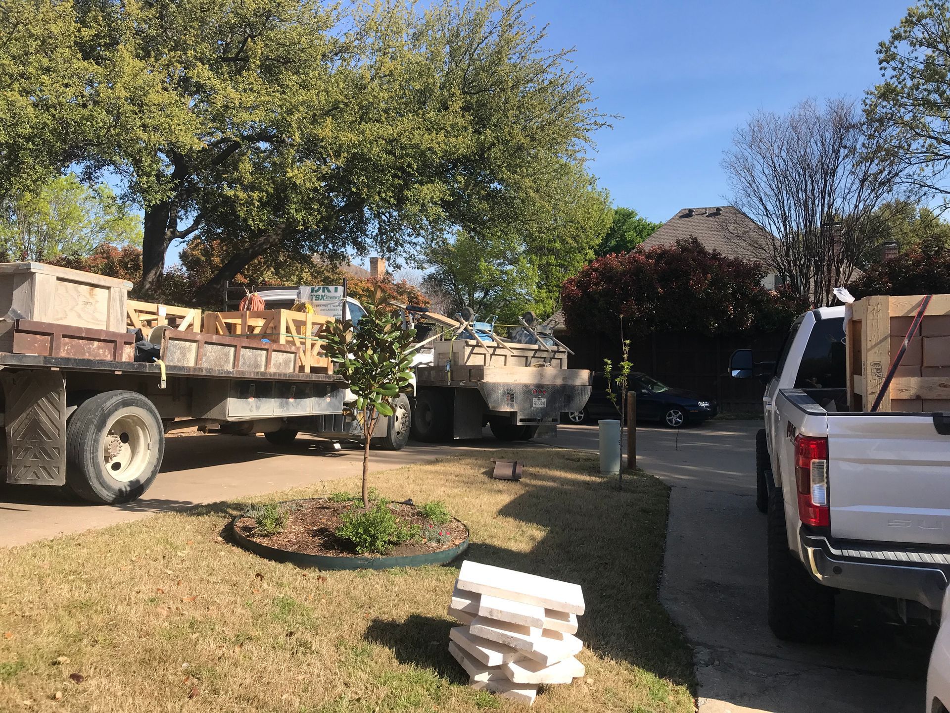 A white truck is parked in a driveway next to a dump truck.