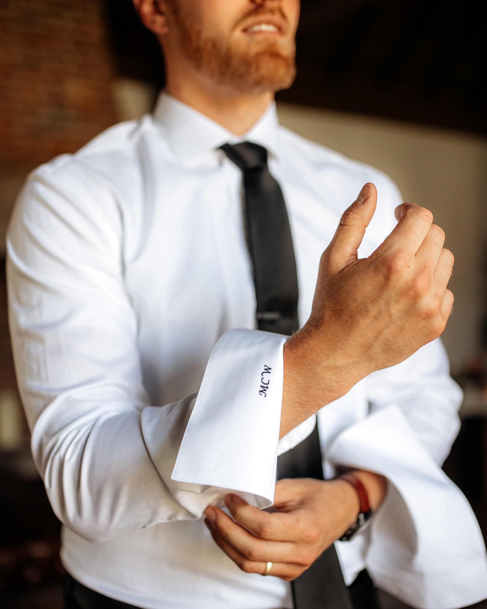 A man in a white shirt and black tie is adjusting his cufflinks