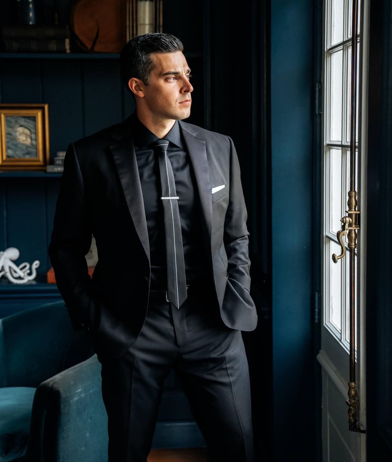 A man in a suit and tie is standing in front of a window.