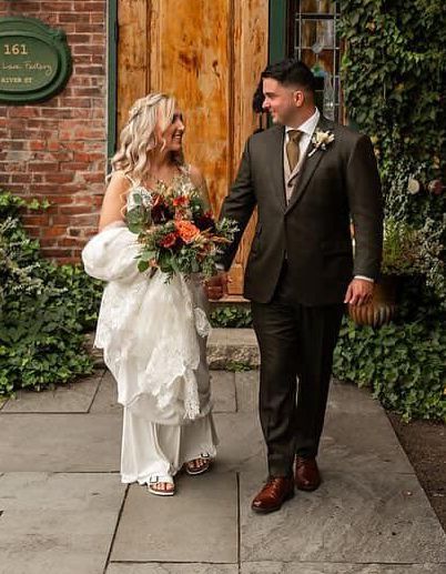 A bride and groom are walking down a sidewalk holding hands.