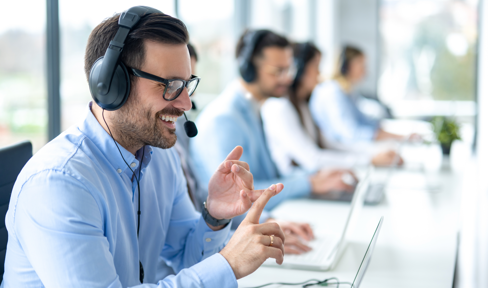 A man wearing headphones is sitting at a desk in a call center.