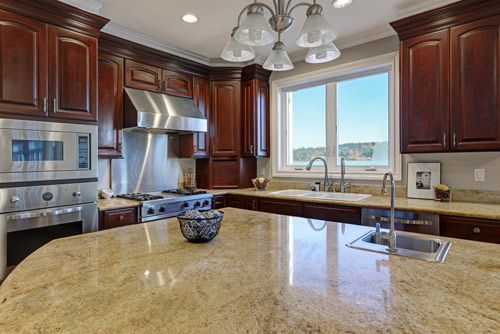 A kitchen with granite counter tops , stainless steel appliances , wooden cabinets and a large island.
