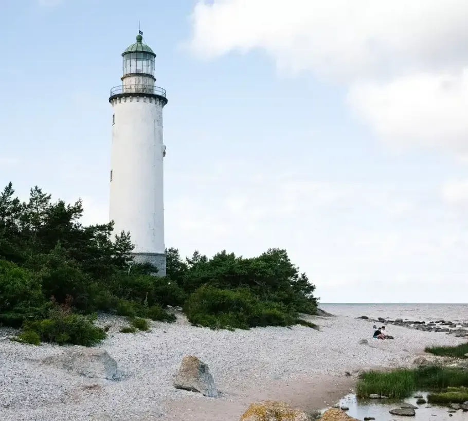 A white lighthouse sits on the shore of a beach