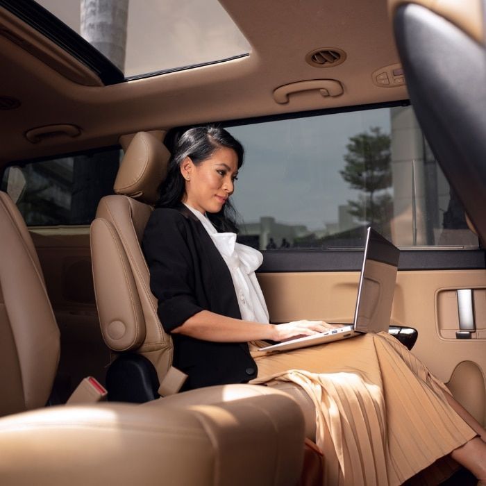 A woman sits in the back seat of a car using a laptop