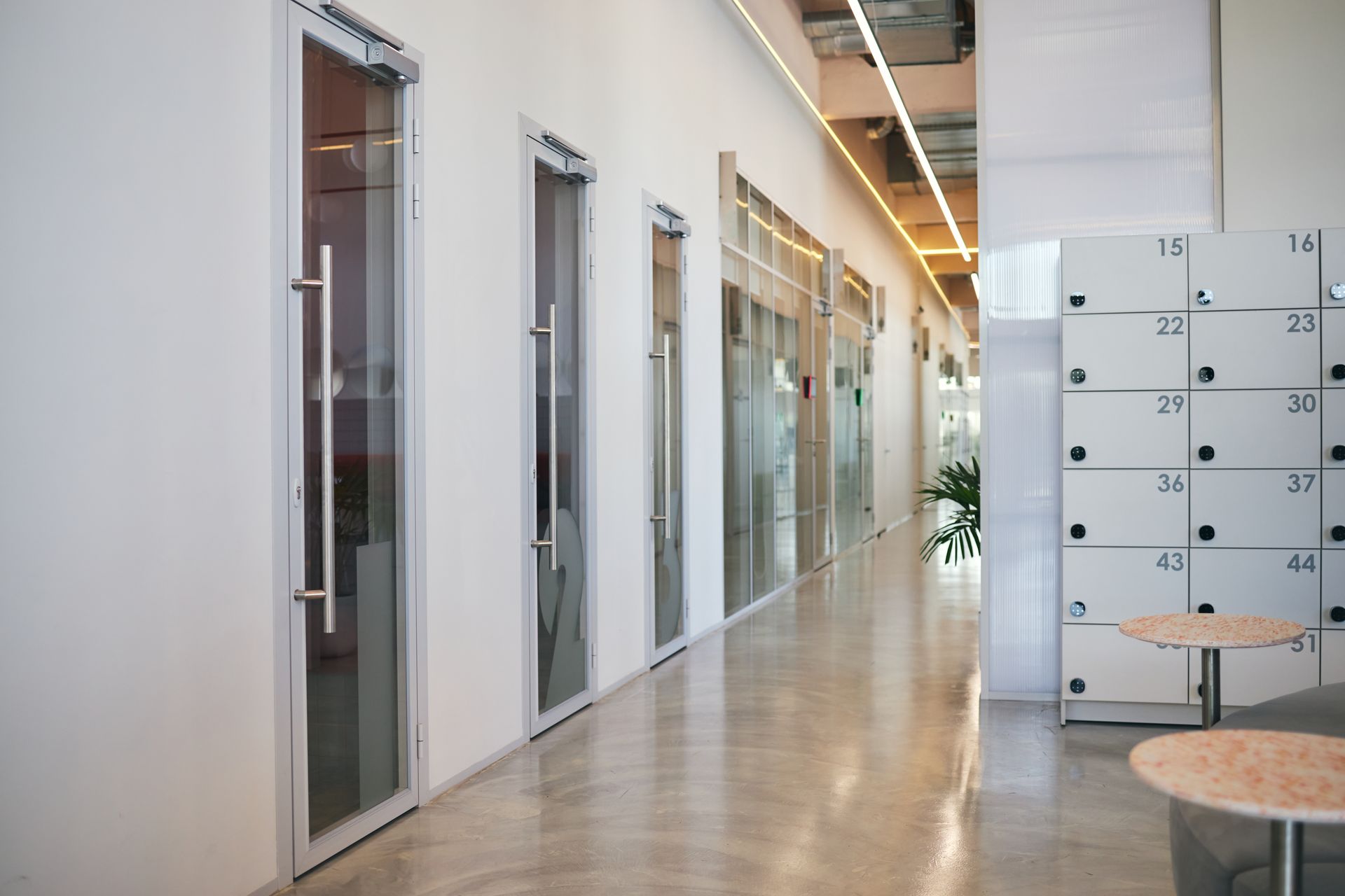 Modern office corridor with glass doors, lockers, and a polished floor