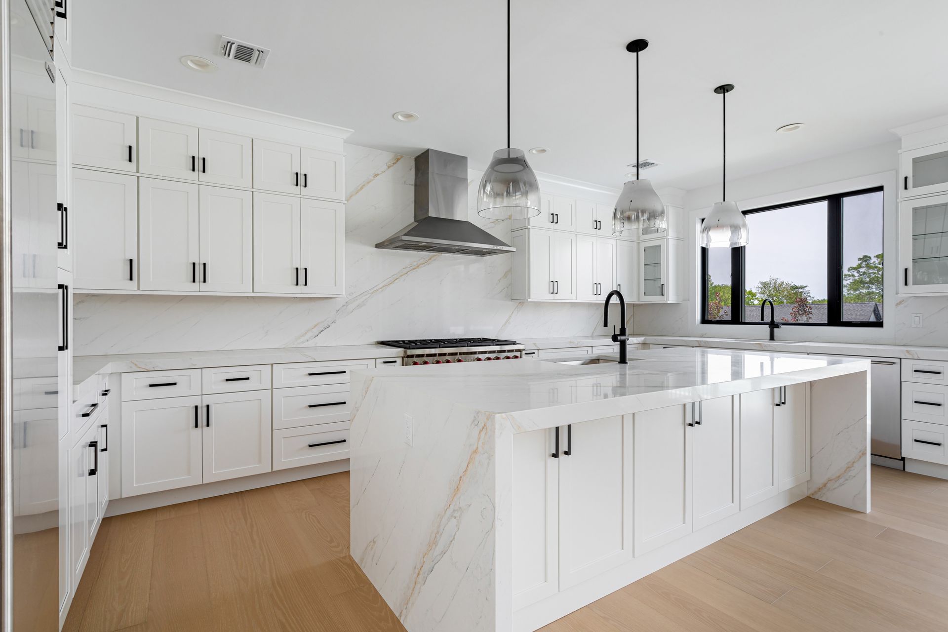 Bright modern white kitchen with marble island, stainless fixtures, and large windows Bright modern white kitchen with marble island, stainless fixtures, and large windows
