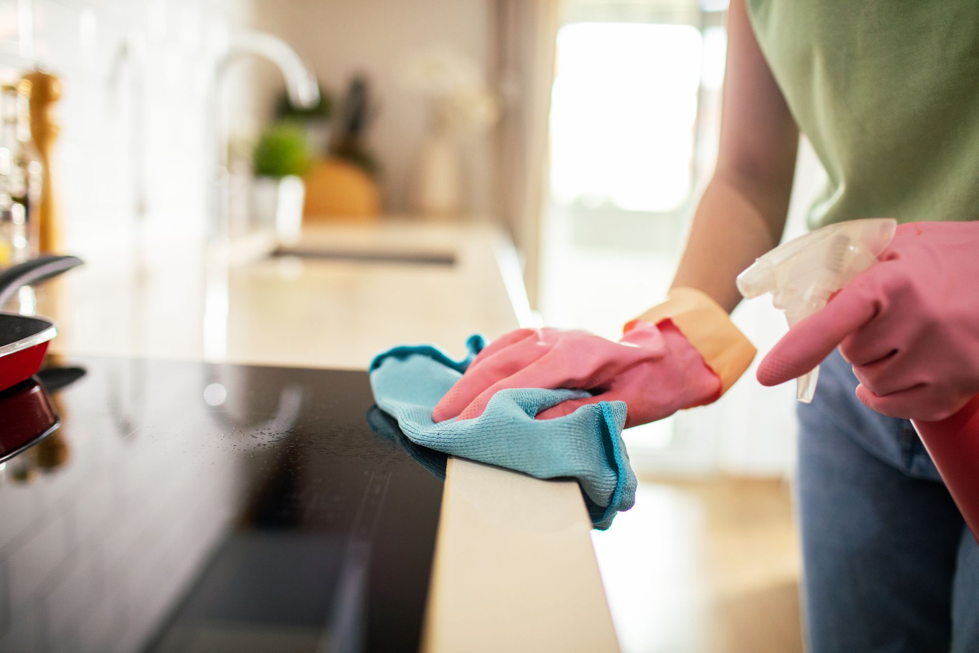 Person wearing pink gloves wiping a countertop with a blue cloth in a kitchen