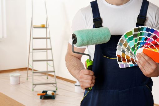 Person holding paint roller and color swatches in a room with a ladder and paint supplies Person holding paint roller and color swatches in a room with a ladder and paint supplies