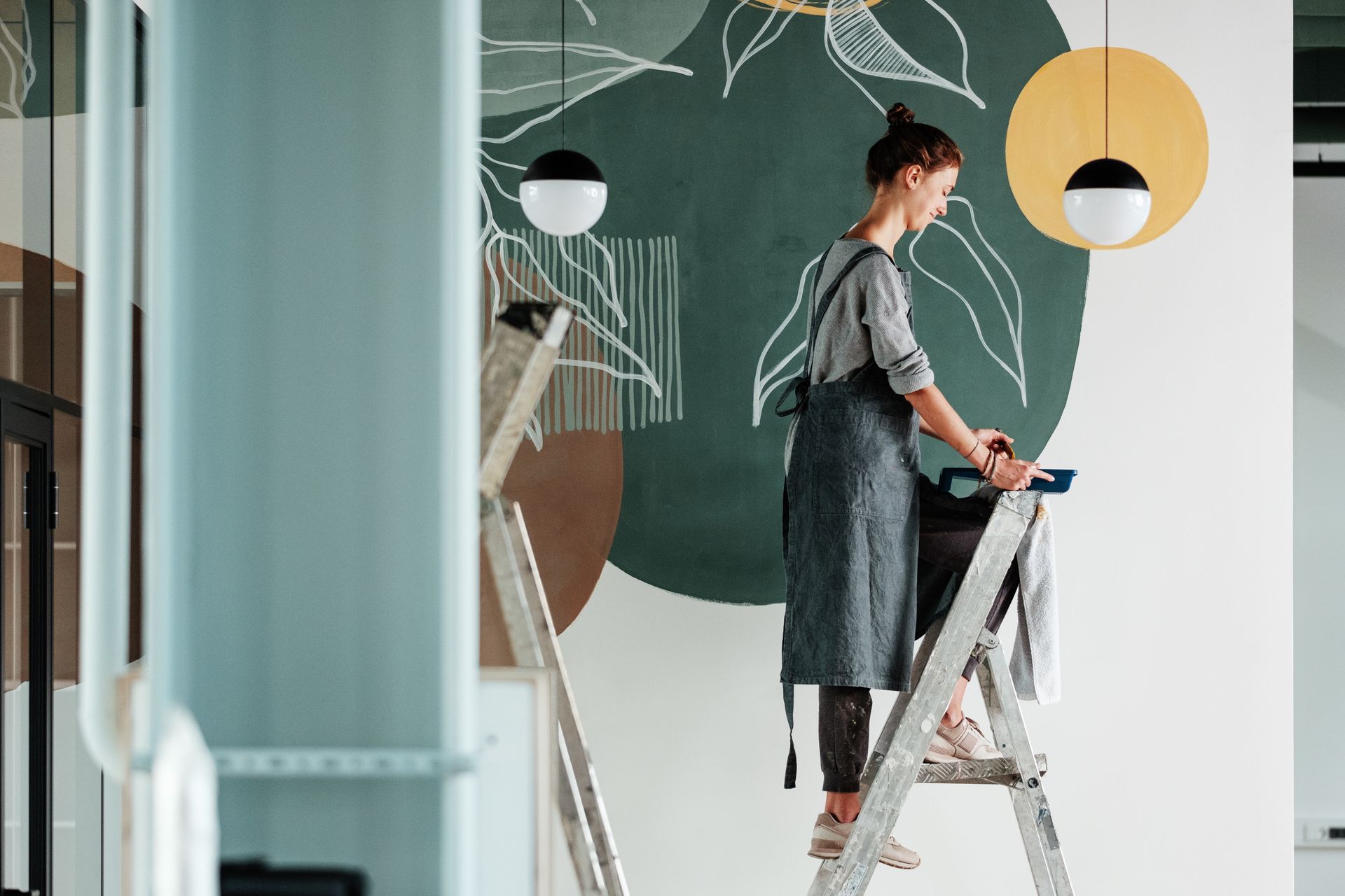 Person painting a wall with chalkboard-style mural in a bright room