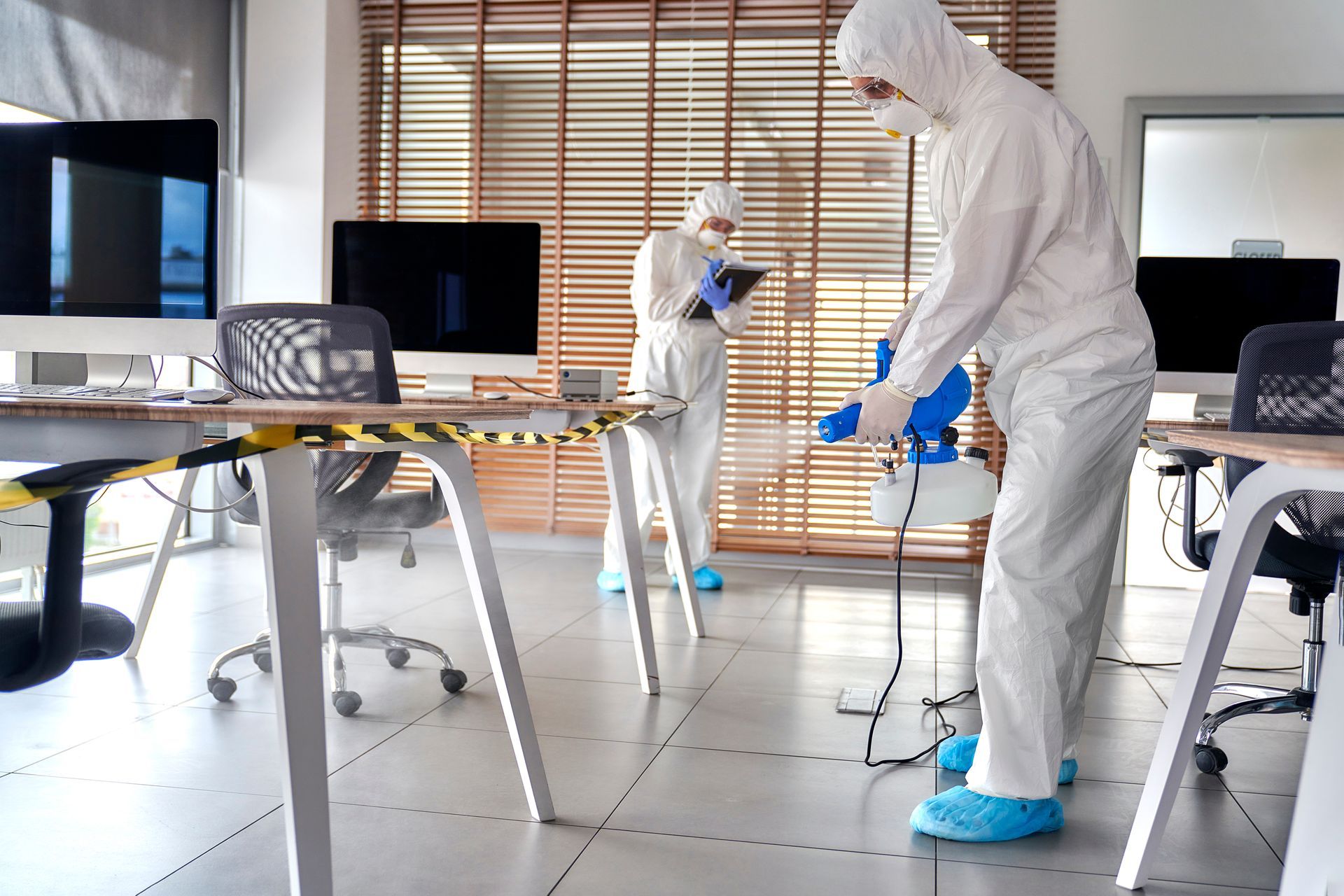 People in white hazmat suits and blue gloves disinfecting an office with spraying equipment People in white hazmat suits and blue gloves disinfecting an office with spraying equipment