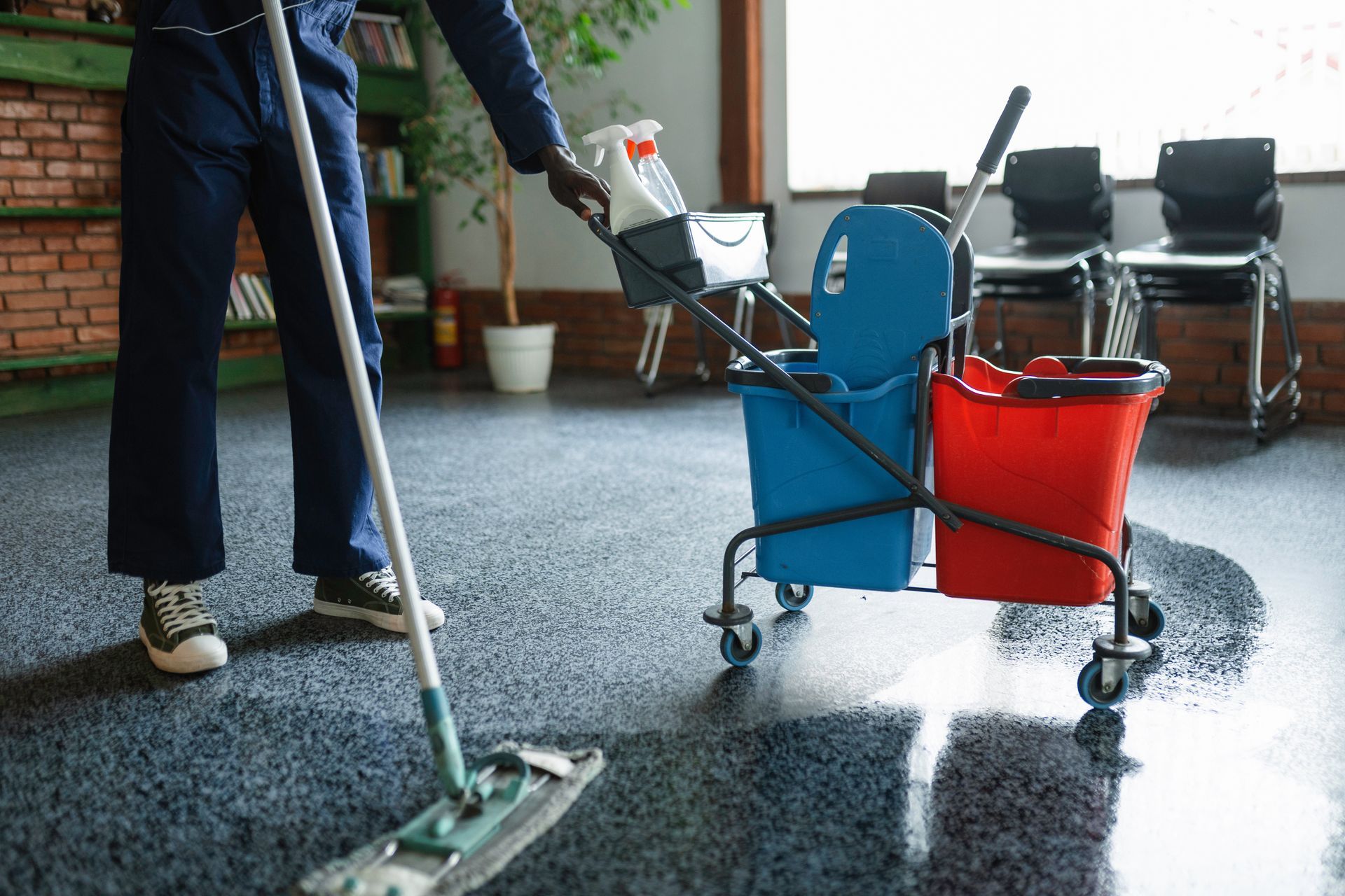 Person mopping a wet patio beside a blue and red cleaning cart with supplies. Person mopping a wet patio beside a blue and red cleaning cart with supplies.