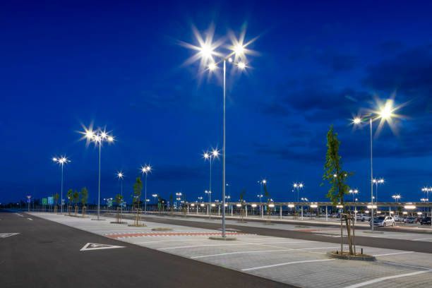 An empty parking lot illuminated by bright streetlights against a deep blue twilight sky.