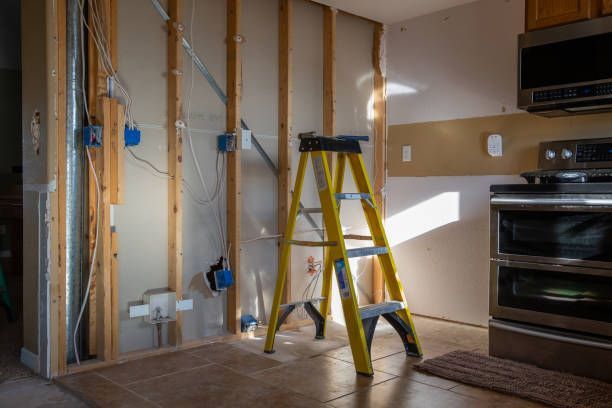 A kitchen renovation in progress featuring open wall studs, exposed electrical wiring, blue boxes, and a yellow stepladder.