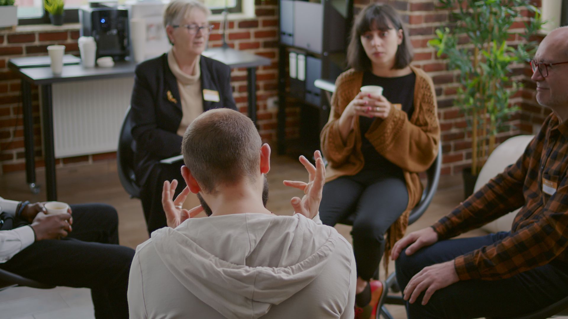 Group anger management therapy with five adults sitting and listening to a man share his experience 