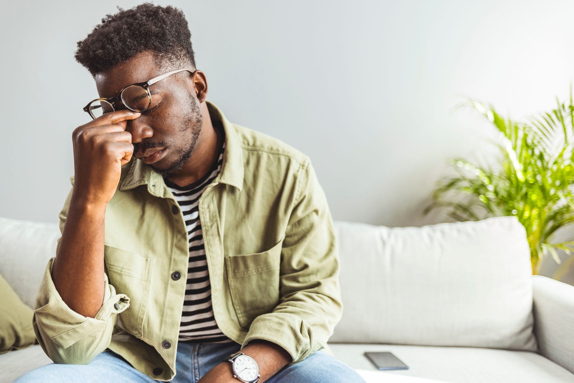 Young man with anxiety as he sits on the couch, pinching the bridge of his nose