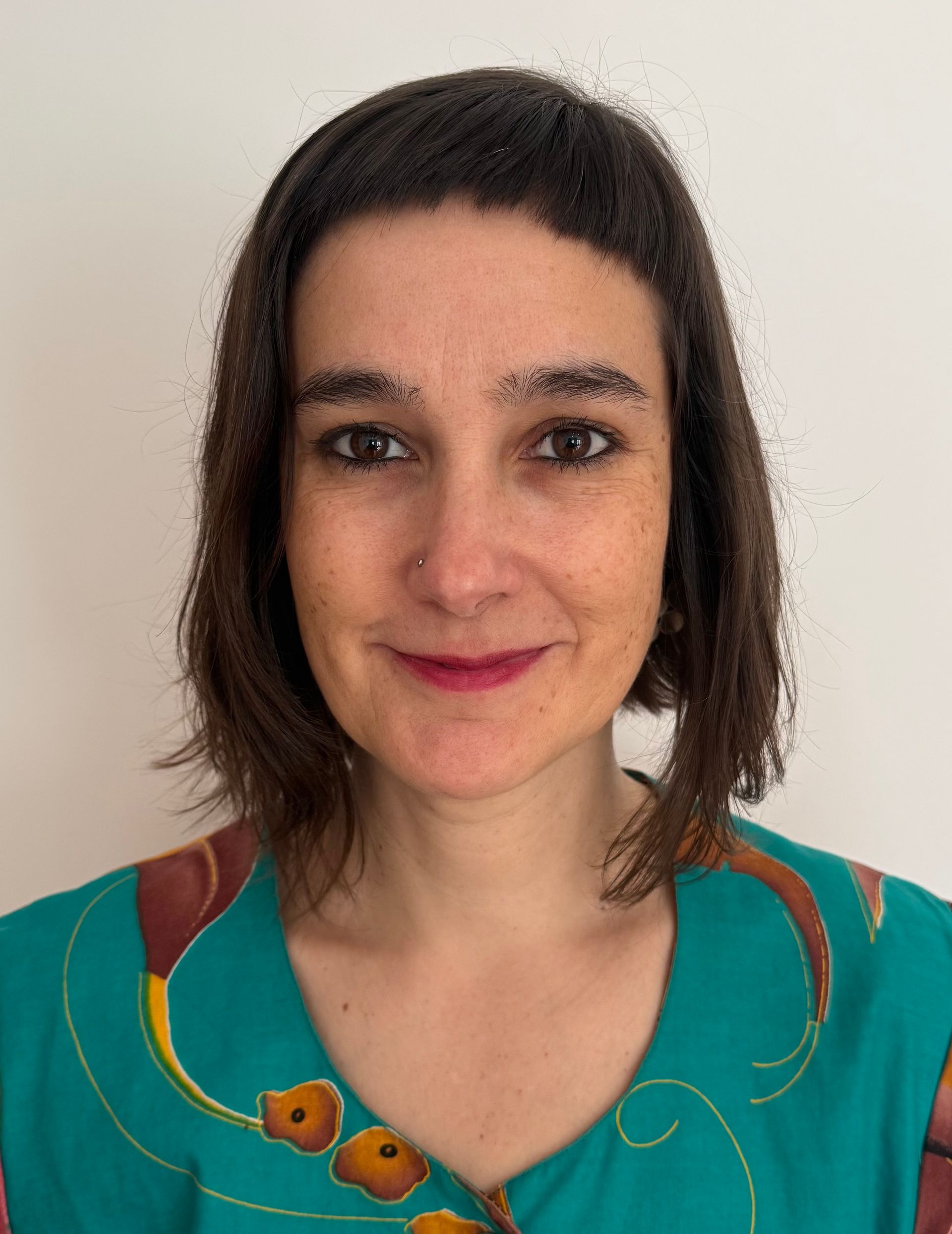 Woman with brown hair smiles, wearing a black blazer and white shirt.