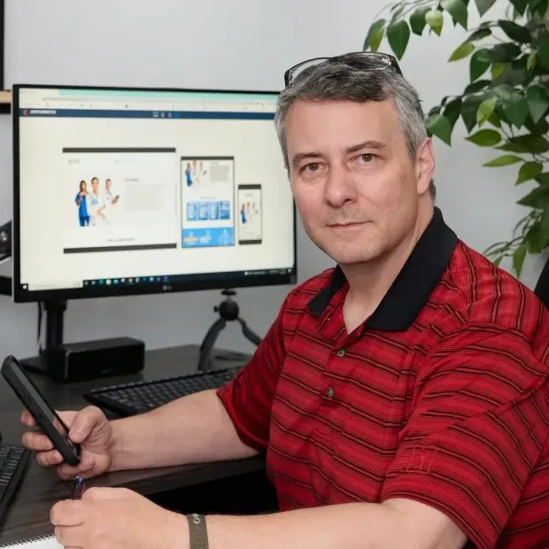 A man in a red shirt is sitting in front of a computer