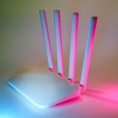 A white router with pink and blue antennas is sitting on a table.