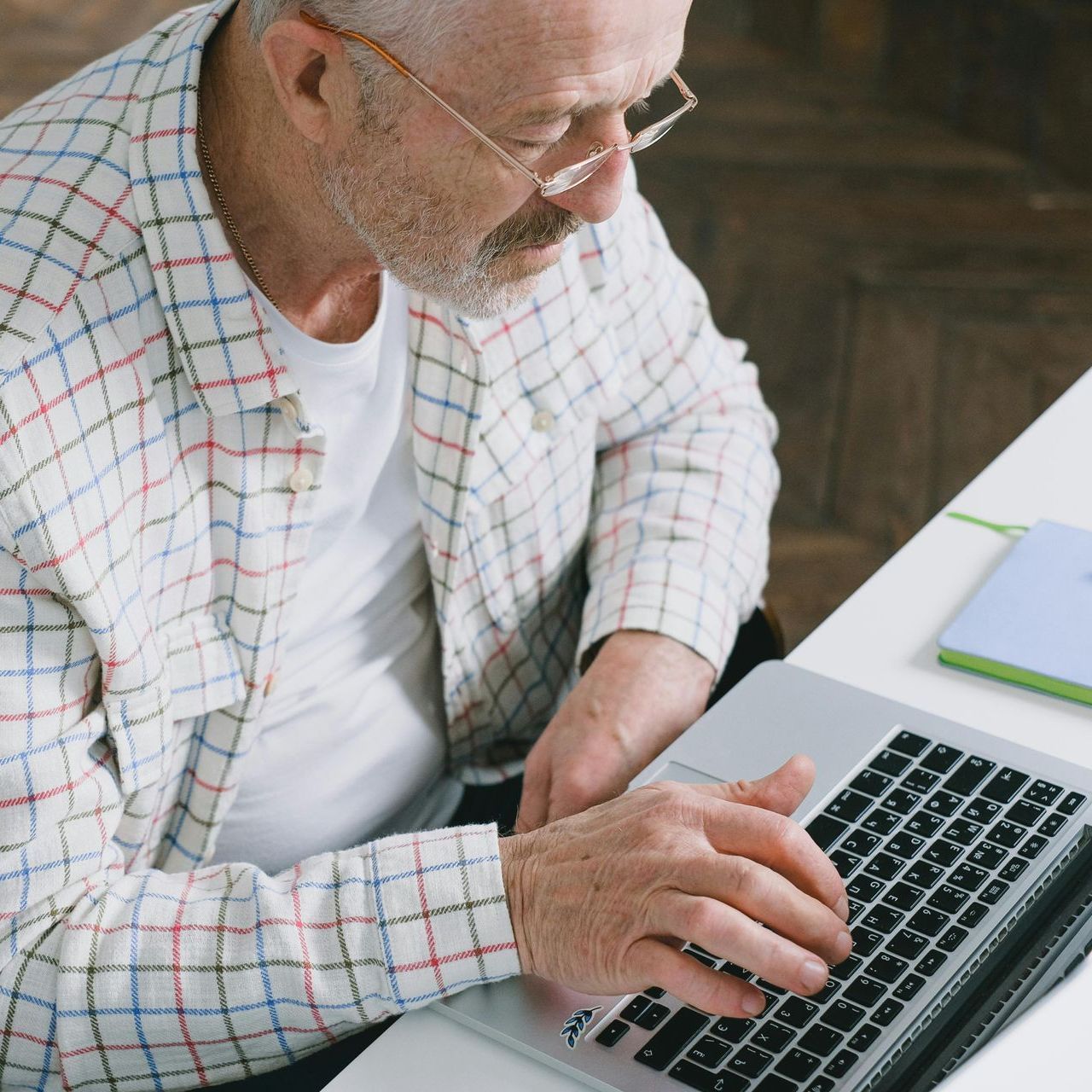 An older man is sitting at a desk using a laptop computer.