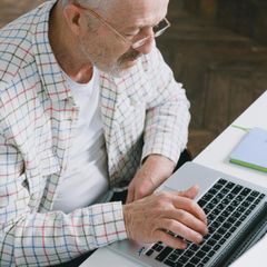 An older man is sitting at a desk using a laptop computer.