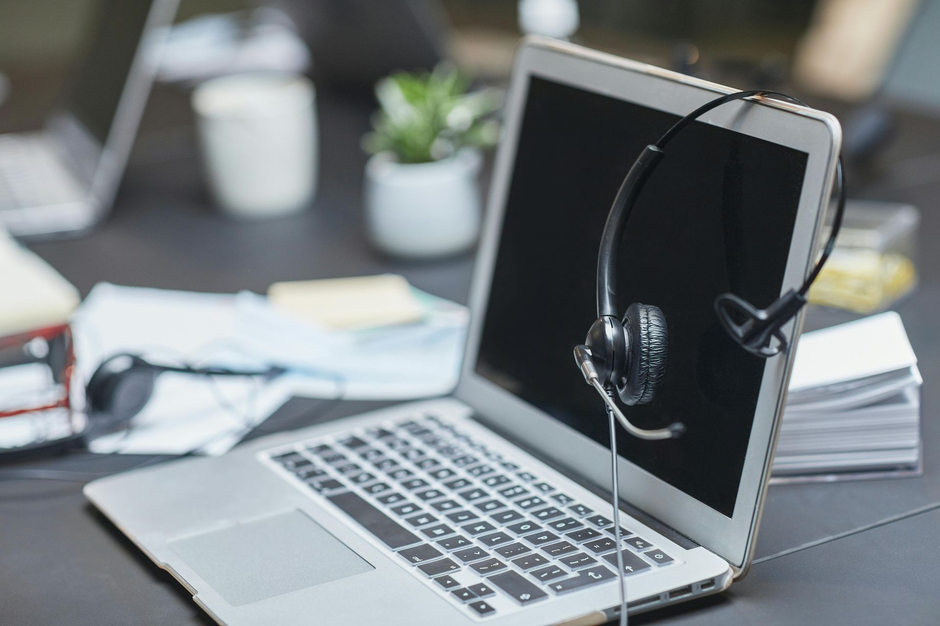 A laptop with a headset on it is open on a desk.