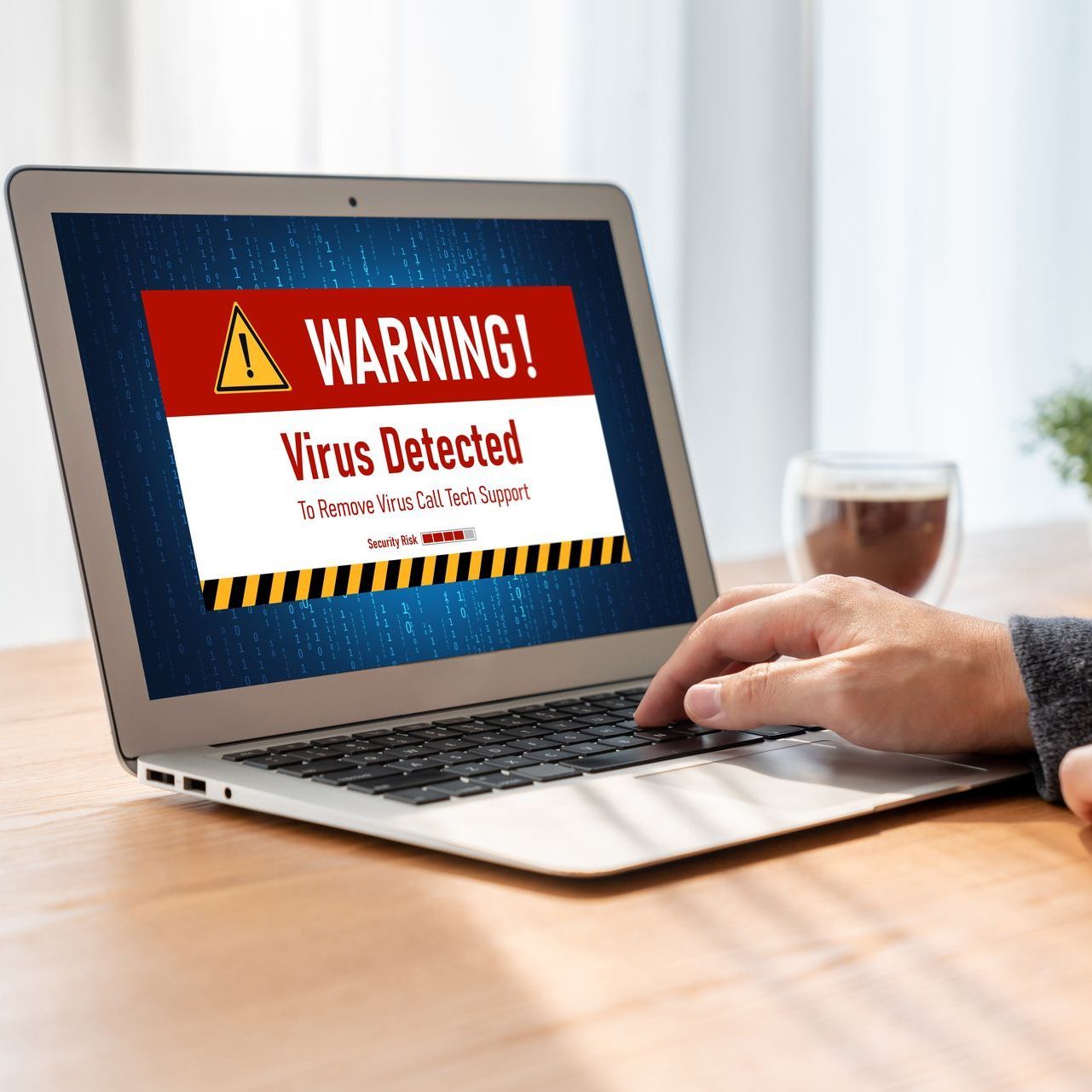 A person is using a laptop computer with a virus warning sign on the screen.
